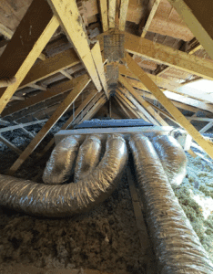 Intérieur sombre d'un grenier avec charpente en bois, isolation en fibre et conduits de ventilation souples et brillants reliés à une boîte centrale.